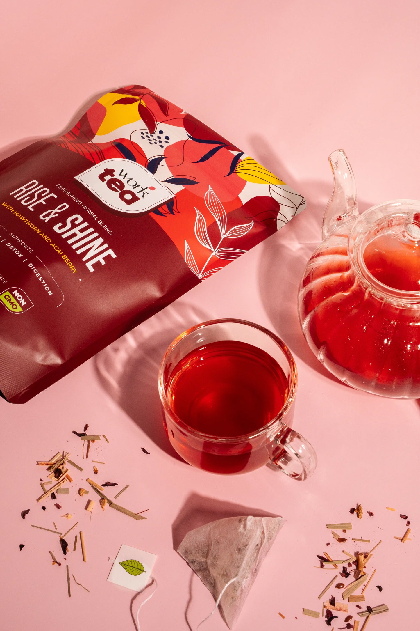 Red tea bag labeled 'Age & Shine' with a glass of red tea and teapot on a pink background