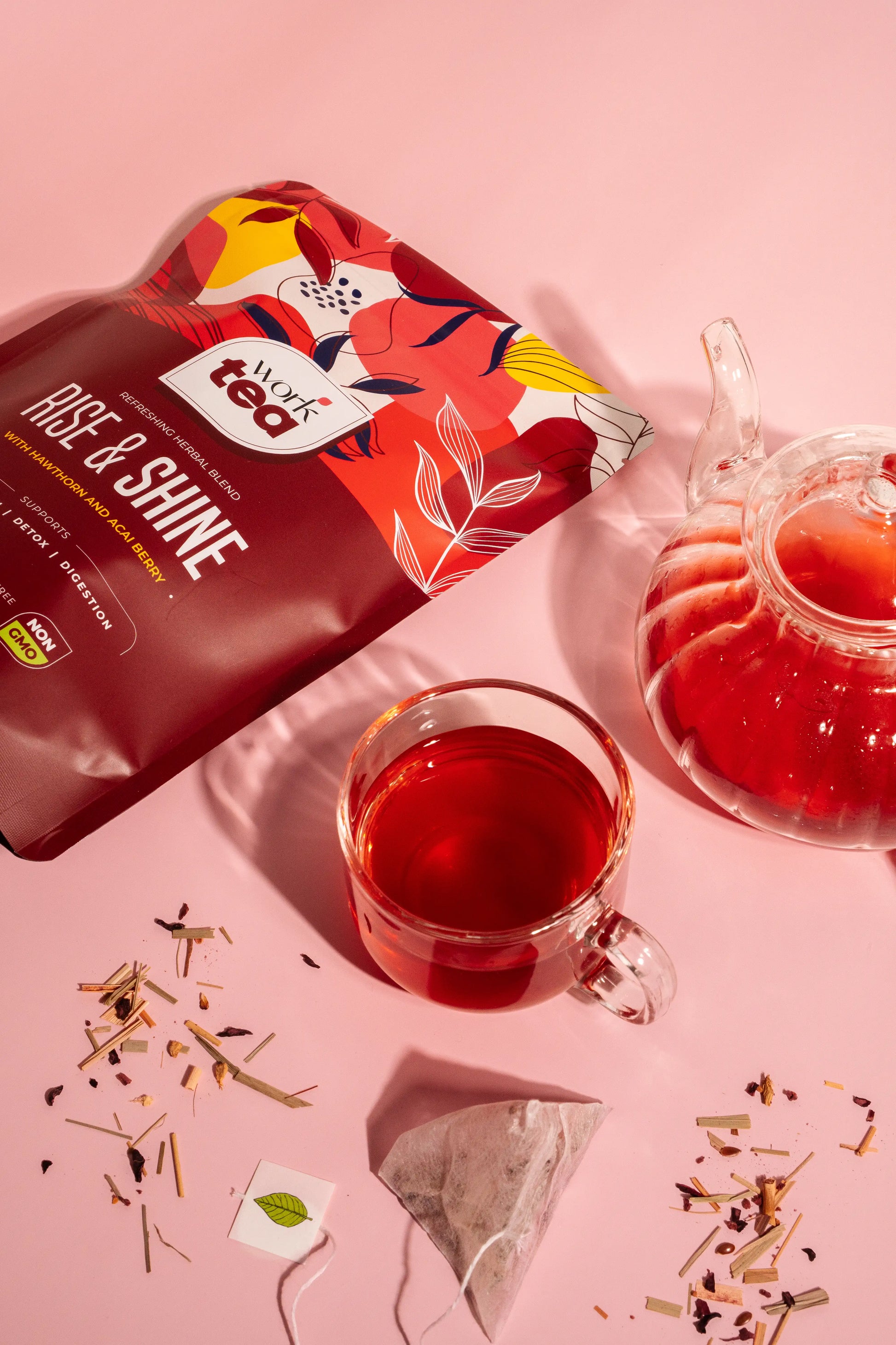 Red tea bag labeled 'Age & Shine' with a glass of red tea and teapot on a pink background